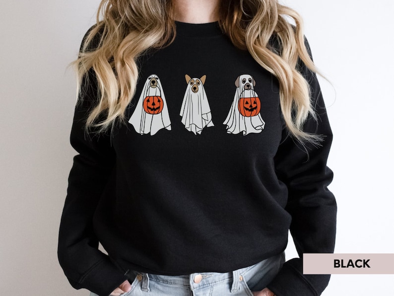 Peut inclure: Sweat-shirt noir avec un motif de trois chiens habill&eacute;s en fant&ocirc;mes tenant des citrouilles. Le texte "BLACK" est visible dans le coin inf&eacute;rieur droit de l'image.