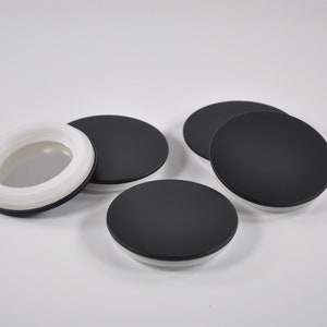 May include: Four round black lids with a white inner ring. One lid has a white mesh insert.