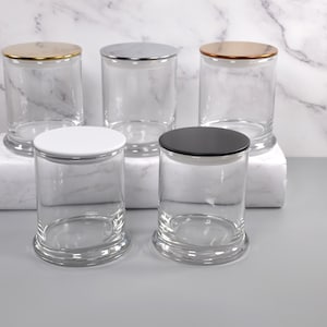 May include: Five clear glass candle jars with different colored lids. The lids are gold, silver, copper, white, and black.