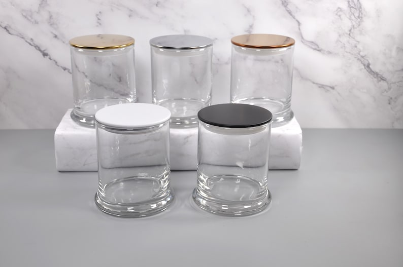 May include: Five clear glass candle jars with different colored lids. The lids are gold, silver, copper, white, and black.