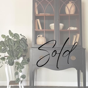 May include: A black painted antique hutch with glass doors and shelves. The hutch has a wood top and a lower cabinet with a drawer. The hutch is sold.