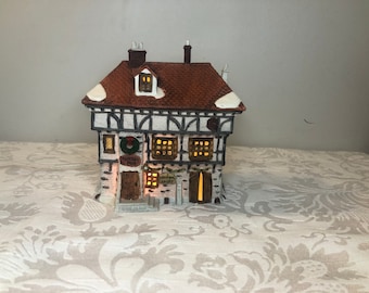 May include: A miniature ceramic building with a brown roof, white trim, and a stone facade. The building has lit windows and a sign that reads "Furthest Pub". A wreath decorates the front. The overall theme is a Christmas village.