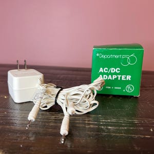 May include: A white AC/DC adapter with a white cord and a green box that says "Department 56 AC/DC Adapter Item # 88036".