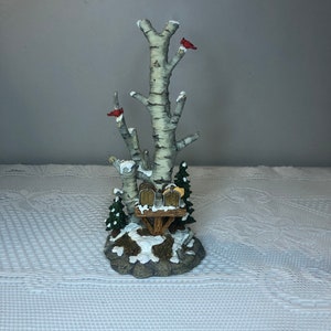 Puede incluir: Una figurita de escena de invierno con dos abedules, dos cardenales rojos y dos buzones sobre una base nevada.