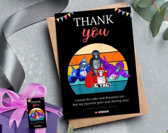 Peut inclure: Carte de remerciement noire avec une illustration de gorilles de dessins animés. La carte porte l'inscription "THANK YOU" en blanc et rouge, avec du texte supplémentaire en dessous. Un coffret cadeau avec une étiquette assortie est également visible.