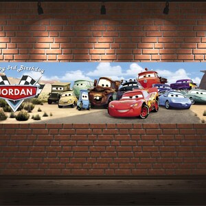 May include: A rectangular horizontal banner featuring a desert landscape with various anthropomorphic cartoon cars. The text reads Happy 3rd Birthday and JORDAN inside a red emblem with checkered flags. The scene includes a red race car.