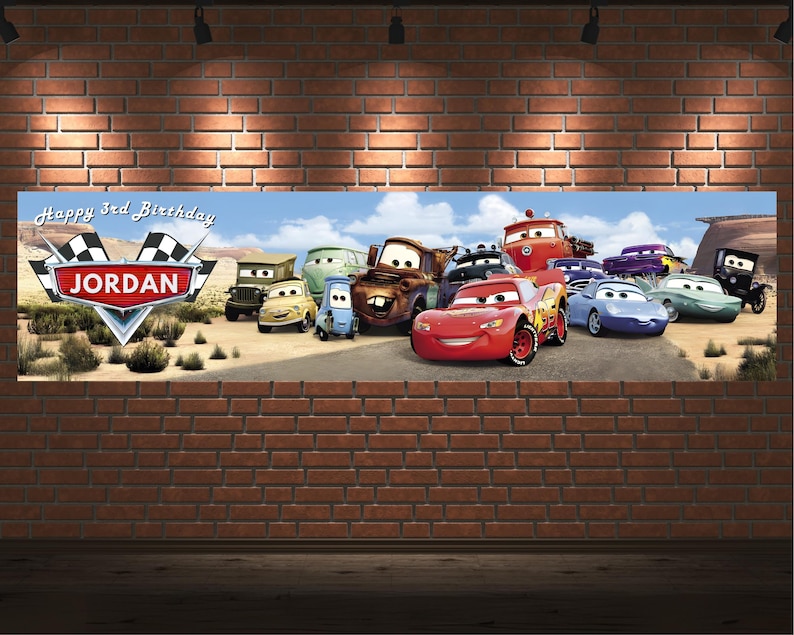 May include: A rectangular horizontal banner featuring a desert landscape with various anthropomorphic cartoon cars. The text reads Happy 3rd Birthday and JORDAN inside a red emblem with checkered flags. The scene includes a red race car.