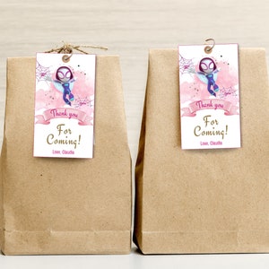 Puede incluir: Dos bolsas de papel marr&oacute;n con etiquetas de agradecimiento rosa y blancas adjuntas. Las etiquetas presentan una imagen de dibujos animados de una ni&ntilde;a vestida como Spider-Man. El texto en las etiquetas dice "&iexcl;Gracias por venir! Con cari&ntilde;o, Claudia."