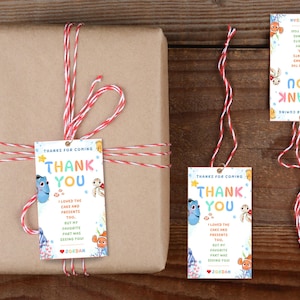 May include: A wrapped present in brown paper, secured with red and white twine. Rectangular tags are attached, featuring the words "Thank You" and cartoon characters. The tags also include the text "Thanks for coming" and a personalized message.