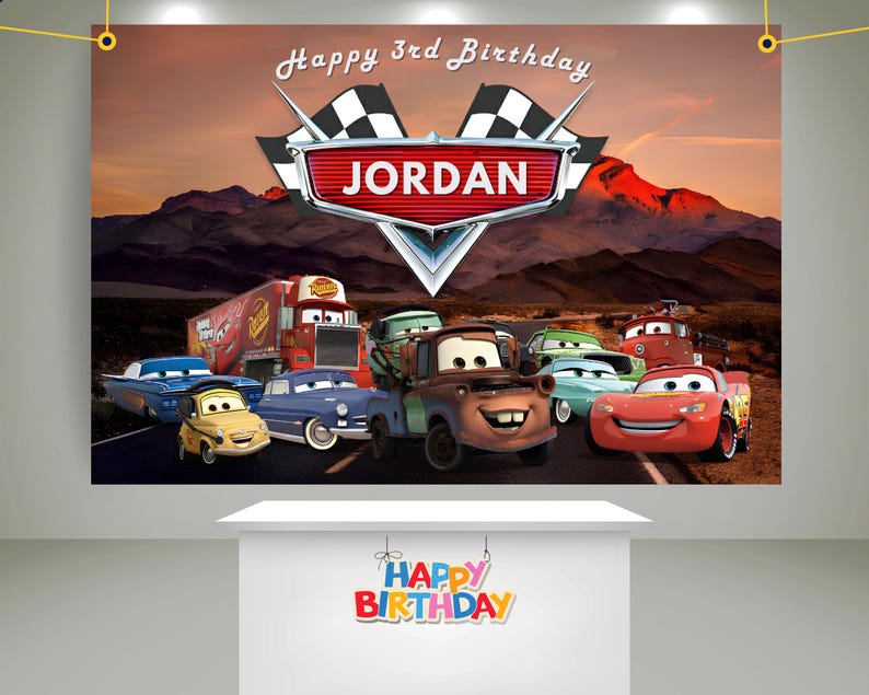 May include: A birthday banner featuring the Cars movie characters with the name "Jordan" in a red emblem. The banner has a mountain backdrop and the text "Happy 3rd Birthday". A smaller sign below reads "Happy Birthday".