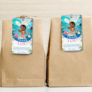 May include: Two brown paper bags with blue and white thank you tags featuring a cartoon character from the movie Moana. The text on the tags reads "Thank You" and "I loved the cake and presents too, but my favorite part was seeing you! for Nolan".
