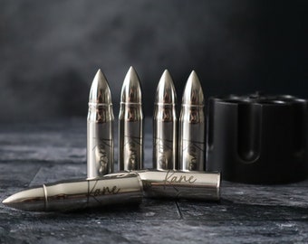 May include: Six silver bullet-shaped ice molds with the name "Kane" engraved on each. The molds are arranged in a row with one lying on its side. A black plastic holder for the molds is in the background.
