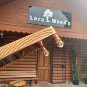 K&ouml;nnte beinhalten: Ein goldfarbenes Tablett aus Metall mit einem dekorativen, erh&ouml;hten Rand und drei Beinen. Das Tablett befindet sich vor einem Holzgeb&auml;ude mit einem Schild, auf dem "Lara Wood's" steht.