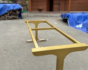 May include: Gold metal table base with a rectangular top and two T-shaped legs. The base is in a rustic setting.