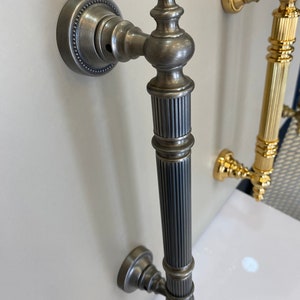 May include: A silver door handle with a fluted design and a decorative knob. The handle is mounted on a white wall.