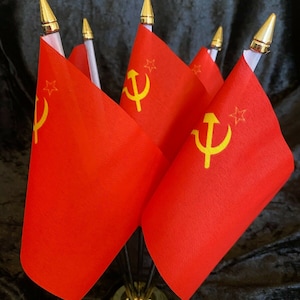 May include: A small display of red flags, each with a yellow hammer and sickle emblem and a star. The flags are mounted on a gold-coloured base with a black stand, and topped with gold finials.