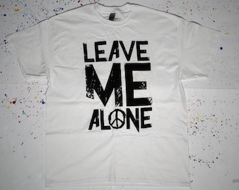 Può includere: Maglietta bianca con testo nero che dice "LEAVE ME ALONE" con un simbolo di pace al centro della parola "ALONE".