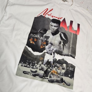 May include: White t-shirt with a black and white photo of Muhammad Ali boxing. The text "Float like a butterfly... Sting like a bee" is printed on the shirt.