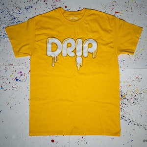 Könnte beinhalten: Ein gelbes T-Shirt mit einem weißen "Drip"-Motiv. Die Buchstaben sind so gestaltet, dass sie wie tropfende Farbe aussehen.