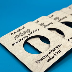 May include: A set of four wooden gift tags with the text "The gift of Nothing absolutely nothing" and "Exactly what you asked for". The tags have a cut-out circle in the center.