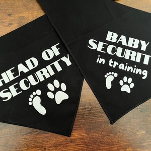 Puede incluir: Dos bandanas negras para perros con huellas blancas y texto. La primera bandana dice "Head of Security" y la segunda bandana dice "Baby Security in training".