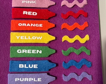 Peut inclure: Un tableau en feutre violet présente des outils d'apprentissage des couleurs. Sept pièces de feutre en forme de crayon, étiquetées "PINK", "RED", "ORANGE", "YELLOW", "GREEN", "BLUE" et "PURPLE", sont disposées avec des pièces ondulées assorties.