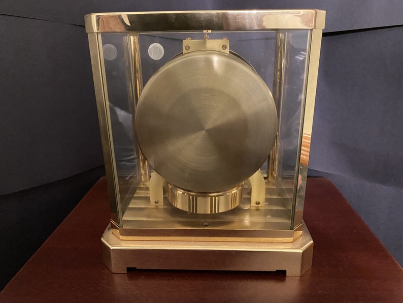 K&ouml;nnte beinhalten: Eine goldfarbene Uhr mit einem Glasgeh&auml;use und einem runden, goldfarbenen Zifferblatt. Die Uhr steht auf einer Holzoberfl&auml;che.