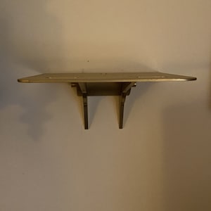 K&ouml;nnte beinhalten: Ein einfaches Holzregal mit zwei Metallkonsolen. Das Regal ist an einer Wand montiert.