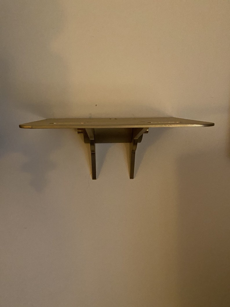 K&ouml;nnte beinhalten: Ein einfaches Holzregal mit zwei Metallkonsolen. Das Regal ist an einer Wand montiert.