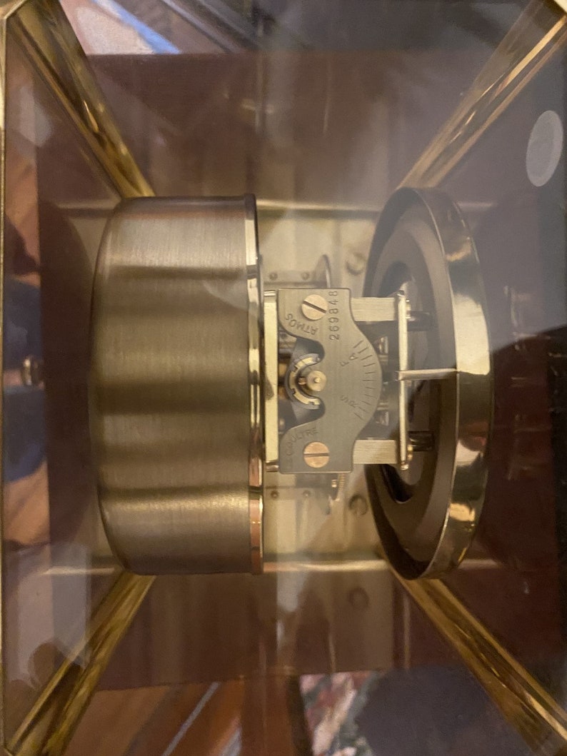 K&ouml;nnte beinhalten: Nahaufnahme eines goldfarbenen Uhrwerks mit einer durchsichtigen Glasabdeckung. Das Uhrwerk hat ein rundes Zifferblatt mit Markierungen und einen kleinen, runden Knopf, auf dem die Nummer "296892" aufgedruckt ist. Der Knopf ist mit "RIMOS" beschriftet.