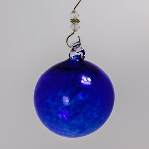 May include: A blue glass Christmas ornament with a white swirl design. The ornament has a gold wire hanger with a clear crystal bead.