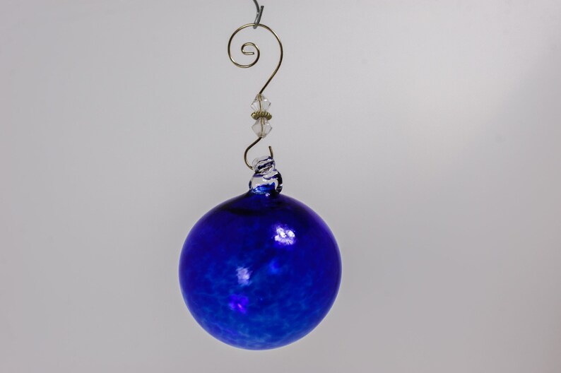 May include: A blue glass Christmas ornament with a white swirl design. The ornament has a gold wire hanger with a clear crystal bead.