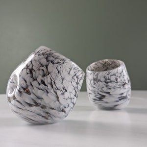 May include: Two white ceramic cups with a black and white marbled design. The cups are tilted at different angles.