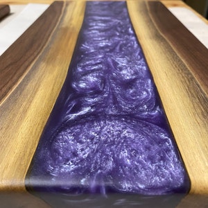 May include: A wooden chopping board with a purple and white resin inlay. The resin has a swirling pattern.