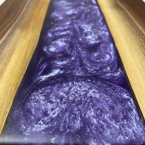 May include: A wooden chopping board with a purple resin inlay. The resin has a swirling pattern and a glittery finish.