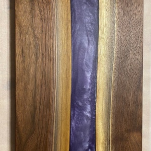 May include: A wooden chopping board with a purple resin inlay. The board has a natural wood finish and is made of walnut wood.