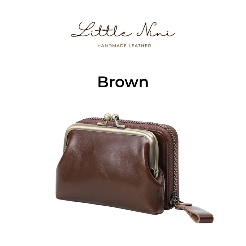 May include: Brown leather wallet with a vintage-style clasp and two zippered compartments. The wallet is made by Little Nini, a brand that specializes in handmade leather goods.