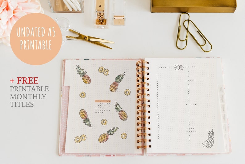 May include: An open A5 spiral-bound planner with pineapple illustrations and the text "UNDATED A5 PRINTABLE" and "+ FREE PRINTABLE MONTHLY TITLES". The planner is open to a dotted grid page with a calendar and a page for notes.