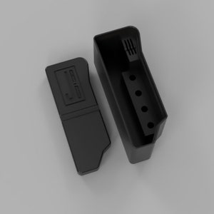 May include: A black rectangular container with a matching lid. The container has a series of holes and slots. The lid has a recessed design. The objects are set against a light gray background.