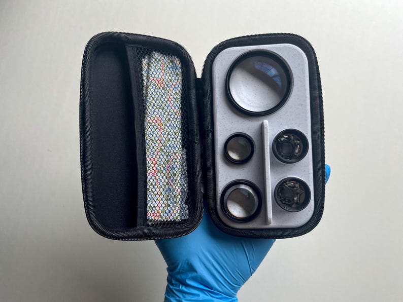 May include: A black zippered case, open to reveal a set of camera lenses and accessories. The case has a gray interior with various lens sizes and a mesh pocket containing a patterned cloth. The lenses are in a variety of sizes.