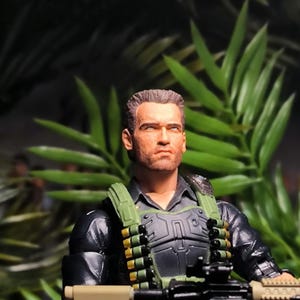 Puede incluir: Primer plano de una figura de acción militar con una chaqueta negra, un chaleco verde y un rifle negro y marrón. La figura tiene una expresión seria en su rostro y lleva una camisa negra debajo de la chaqueta.