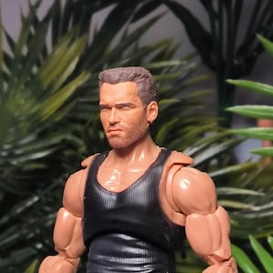 May include: A close-up of a plastic action figure wearing a brown tank top. The figure has a muscular build and a sculpted face with a serious expression.