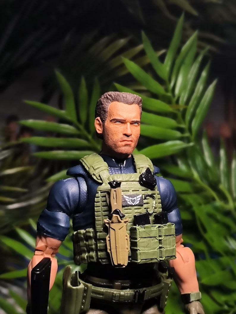 May include: A military action figure wearing a green tactical vest, a black knife, and a black pistol. The figure has short brown hair and a serious expression.