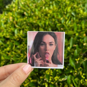 May include: A close-up photo of a woman with dark hair and brown eyes. She is wearing a red shirt and has her tongue sticking out. She is holding a lighter in her hand.