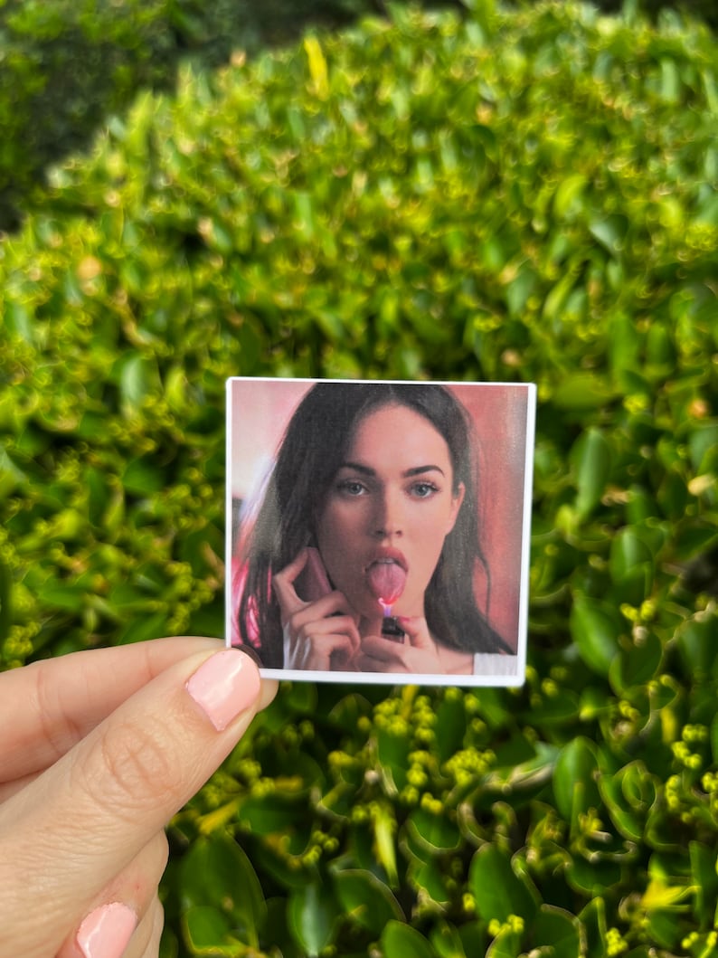 May include: A close-up photo of a woman with dark hair and brown eyes. She is wearing a red shirt and has her tongue sticking out. She is holding a lighter in her hand.