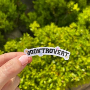 May include: A white sticker with the text "BOOKTROVERT" in black letters. The sticker is decorated with small colorful flowers.
