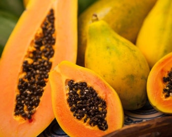 May include: A close-up of several ripe papaya halves, showing the orange flesh and black seeds. The papaya are arranged on a wooden surface with a blue and white patterned design.