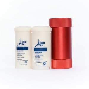 May include: Two white deodorant containers with blue text and a red metal container. The deodorant containers have the text "Deodorant naturel" and "Fabriqué par Ika" on them. The red container has a textured lid.