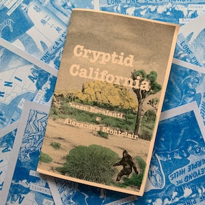 Könnte beinhalten: Ein Taschenbuch mit dem Titel "Cryptid California" mit einer Illustration einer Wüstenlandschaft und einer Bigfoot-Figur. Das Buch ist von blau-weiß bedruckten Ephemeren mit Texten und Kartendesigns umgeben. Autoren: Ocean Escalanti und Alexandra Montclair.