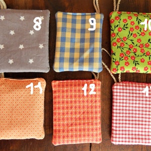 May include: Nine fabric squares with different patterns and colors, numbered 8 through 13. The squares are hanging from strings and are arranged in a row.